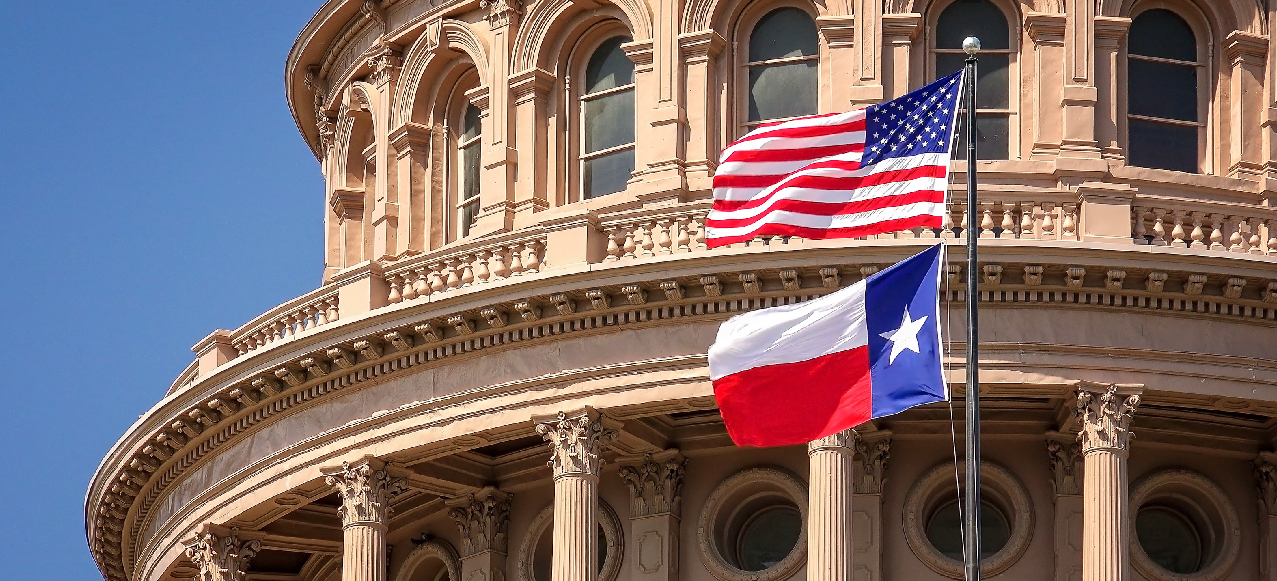 American and Texas state flags flying on the dome of the Texas State Capitol building in Austin